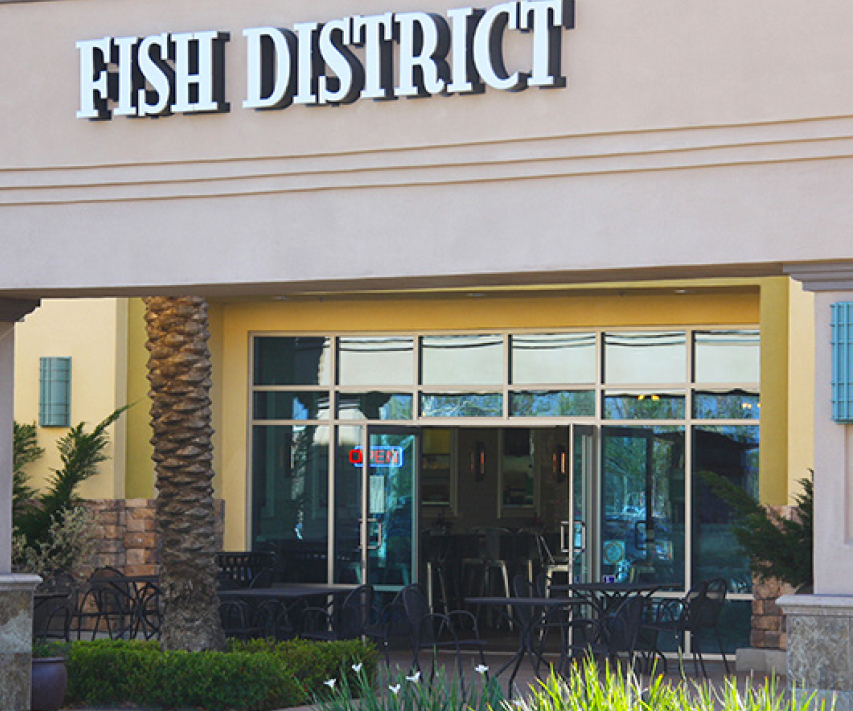 entrance of building with Fish District sign and tables and chairs in front.